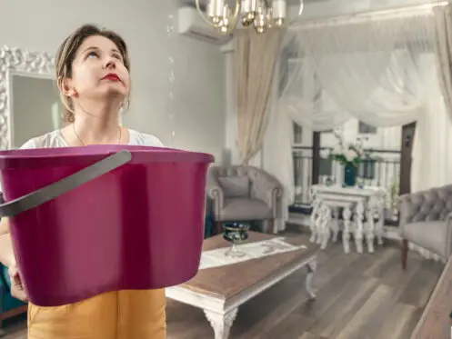 A woman holds a bucket to catch water leaking from the ceiling